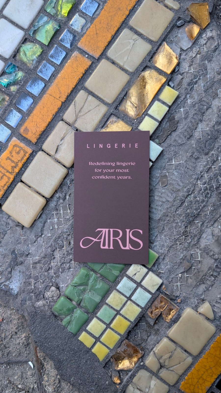 An Airis card resting on a worn mosaic of gold, green and cream tiles